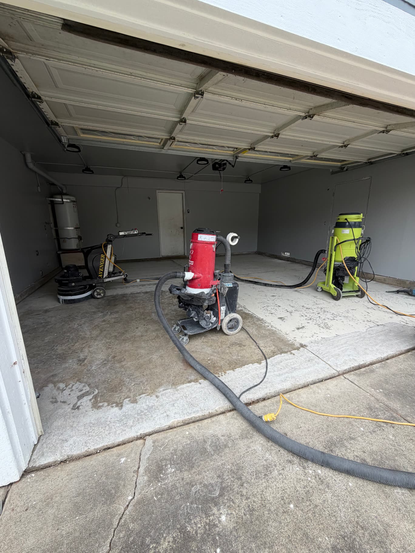 Grinders and vacuums set up in a two-car garage during floor prep