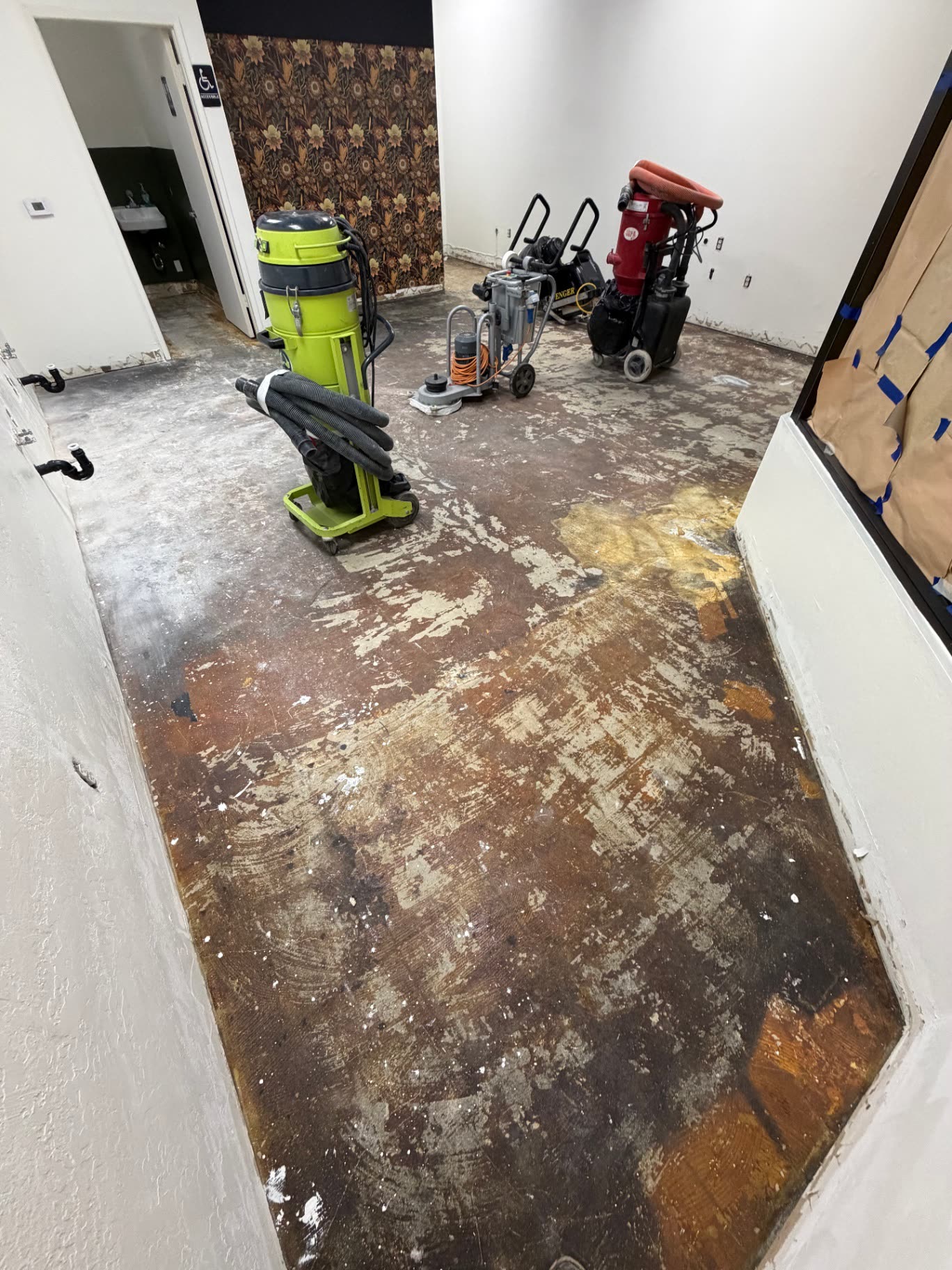 Commercial retail floor stripped to bare concrete with grinding equipment staged