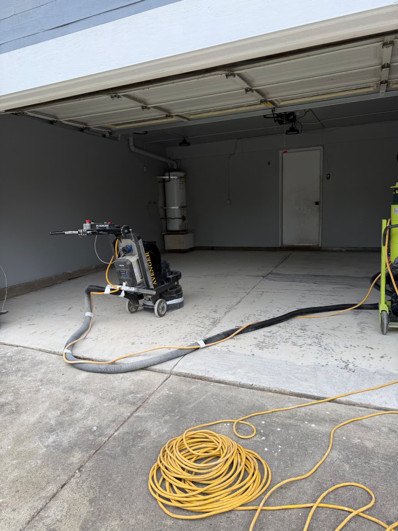 Avenger floor grinder and vacuum in a gray two-car garage during prep