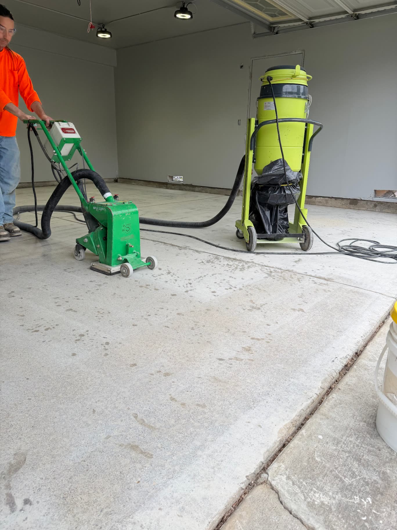Crew member running a scarifier with HEPA vacuum on a garage floor